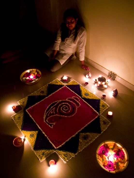 woman kneeling down next to a large colorful rug and lit candles