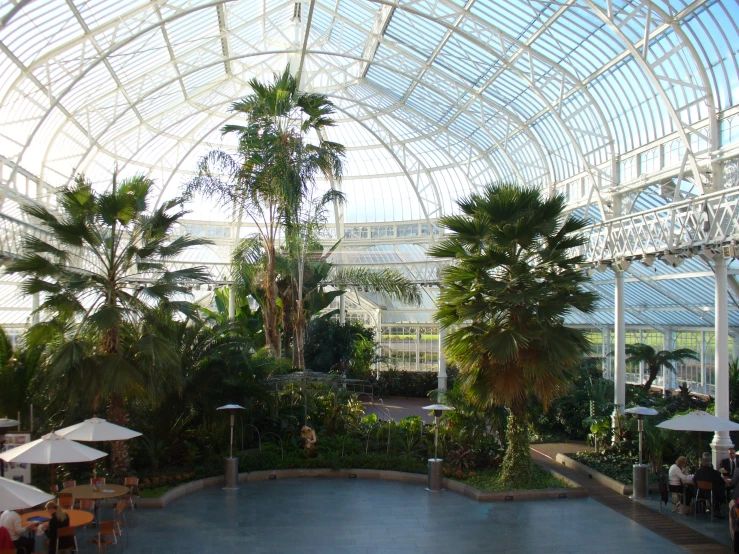 people are sitting in an outdoor restaurant under a big glass roof