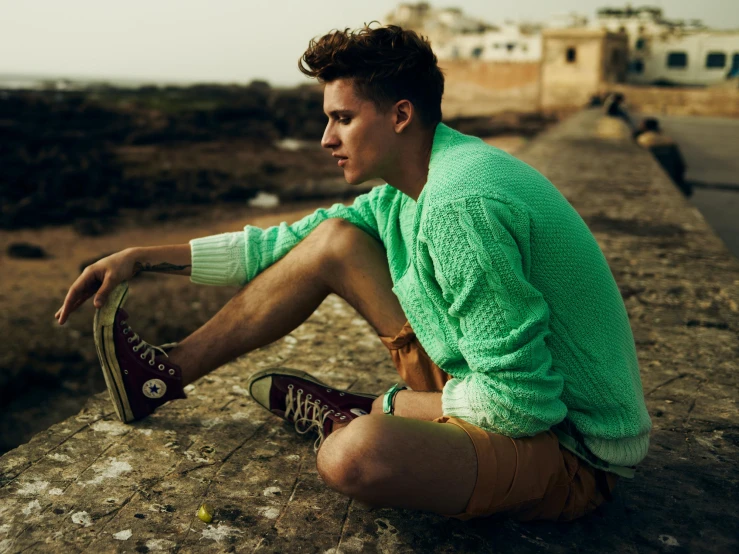 a man sits on a concrete slab holding his shoe while looking off into the distance