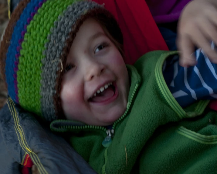 a boy with a green and grey hat sitting in a stroller