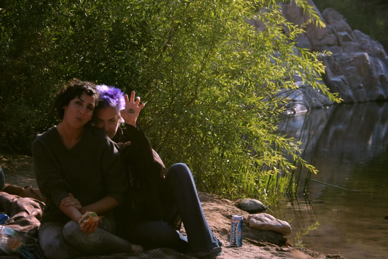 a couple sits on a rock near the water waving