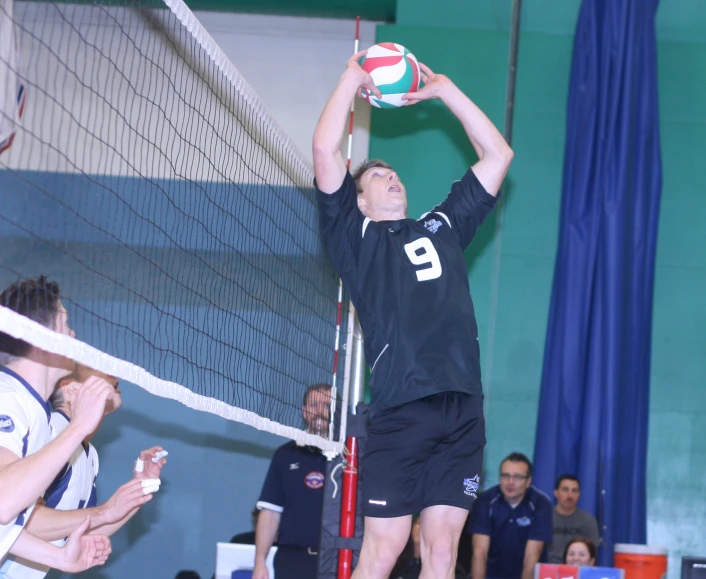 a young man playing volleyball jumps to block the ball