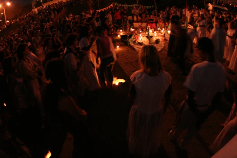 a crowded outdoor event at night with candle lit tables