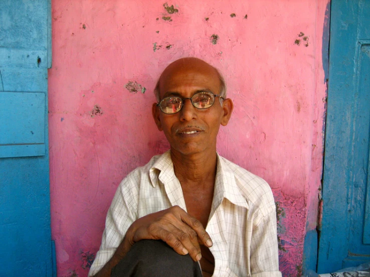 a man sitting on a chair with pink wall behind him