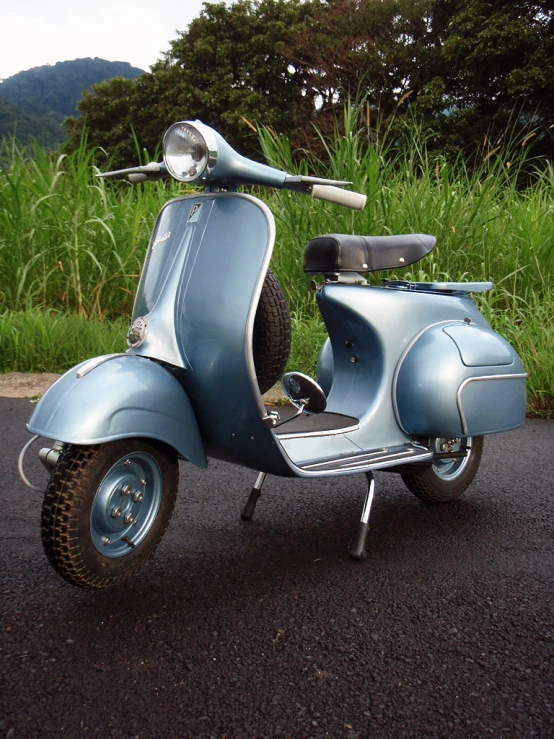 an old, dusty blue vespa sitting by the roadside