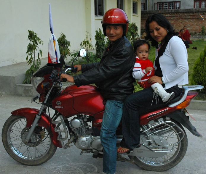 a man and woman with a child on a red motorcycle