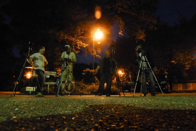 four people standing on grass with telescopes and cameras in hand