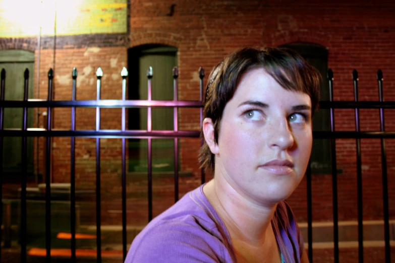 a young woman stands near a fence while staring into the distance