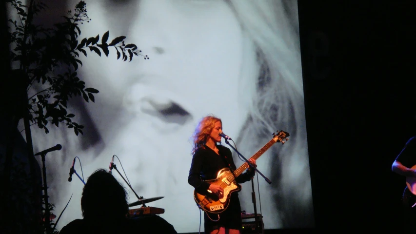 a woman on stage playing a guitar next to a video screen