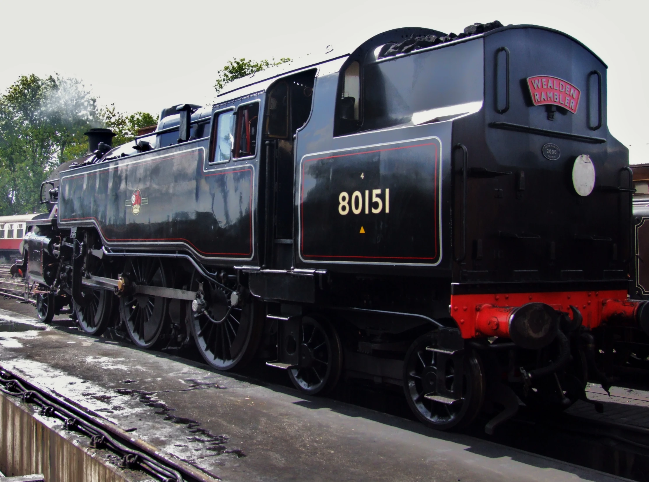 a black train sitting on the tracks and people walking next to it