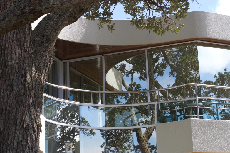 a white wall and circular glass balconies provide privacy to a tree and the circular window of the outside building is visible through which is a tree