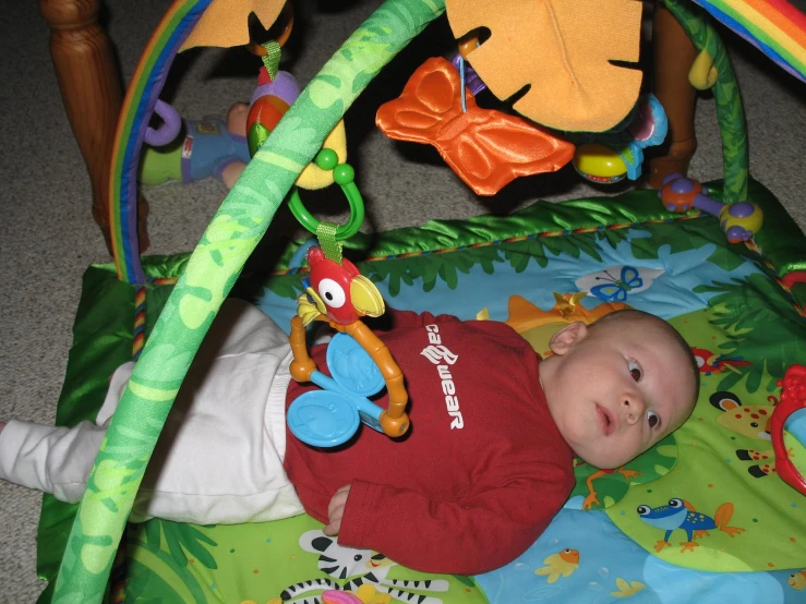 a baby lies in his play mat and looks down