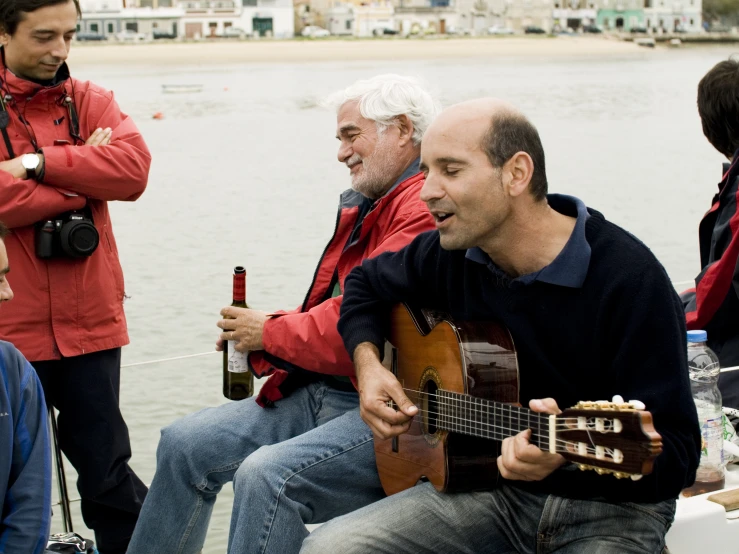 a man playing guitar on a dock next to other people