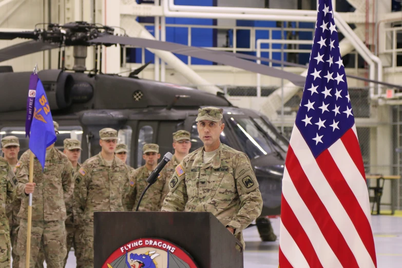 soldiers at a podium in front of a helicopter