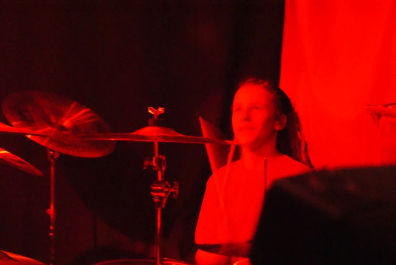 girl playing drums on stage in a red light