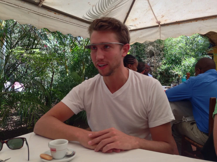 a man wearing clear sunglasses and sitting at a table