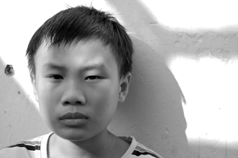 a young asian boy standing against a white wall