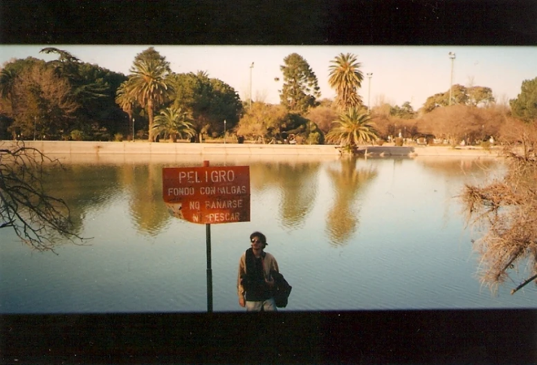 a man standing on the sidewalk next to a sign in front of water