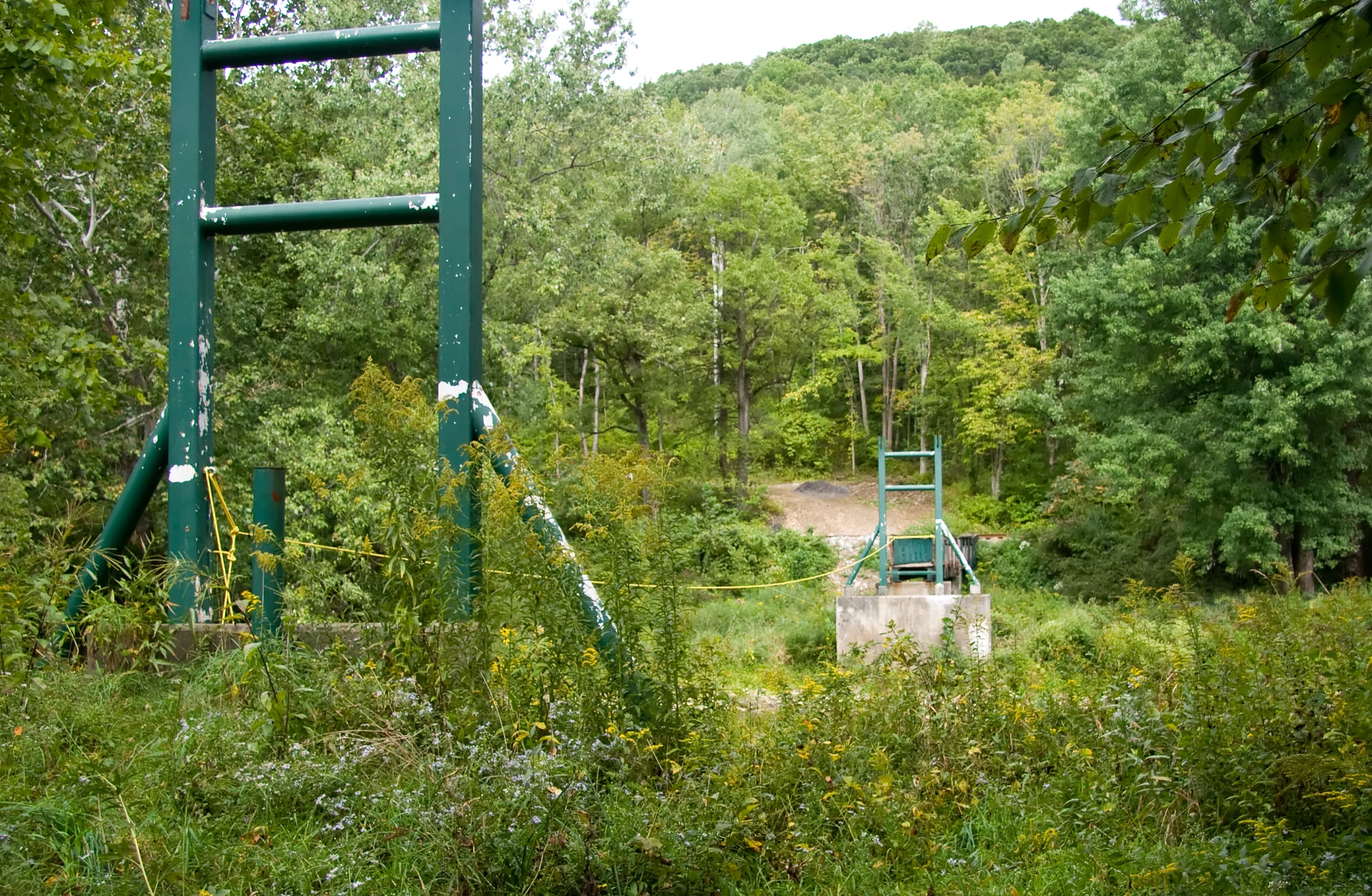 a green metal park bench next to a dirt road