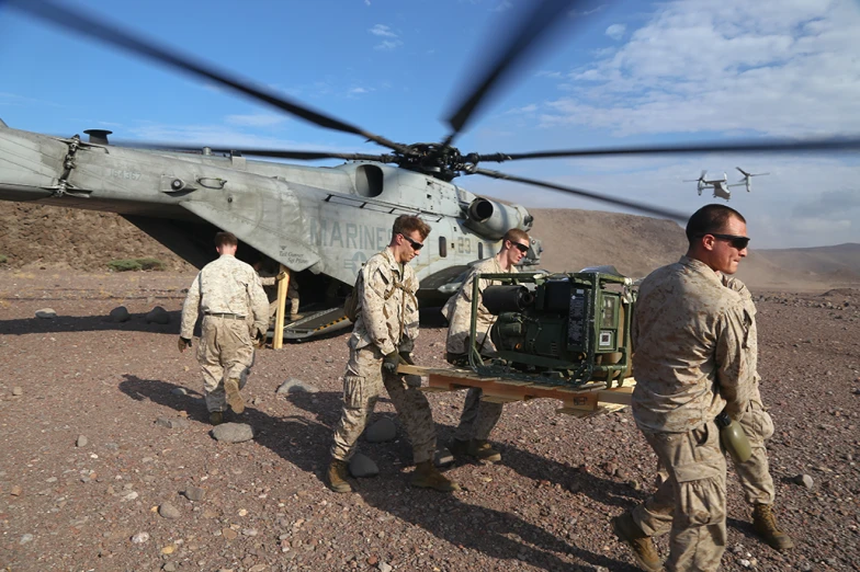 the men are carrying a luggage cart next to a helicopter