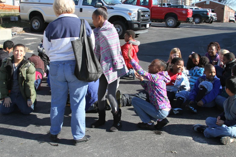 a group of children sitting on the street while a man handing a persons hand