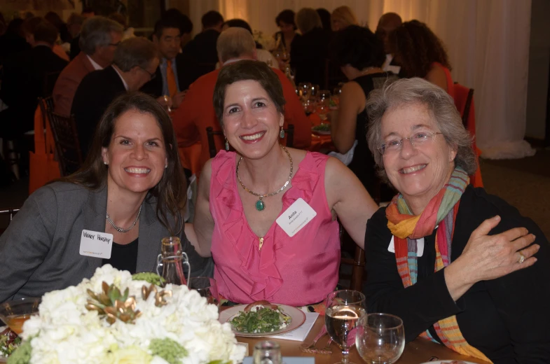 three women are sitting at a table with white flowers