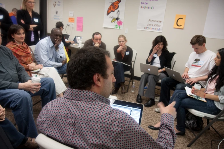 a group of people are gathered in a room with laptops