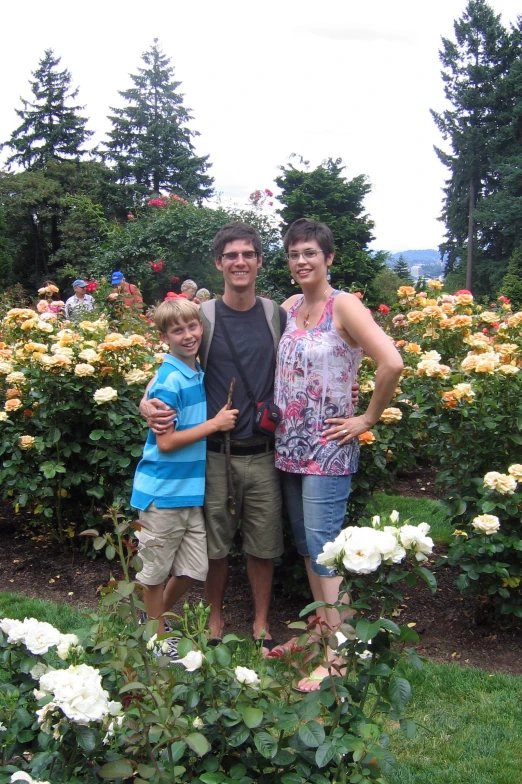 two people posing in a garden next to trees and bushes