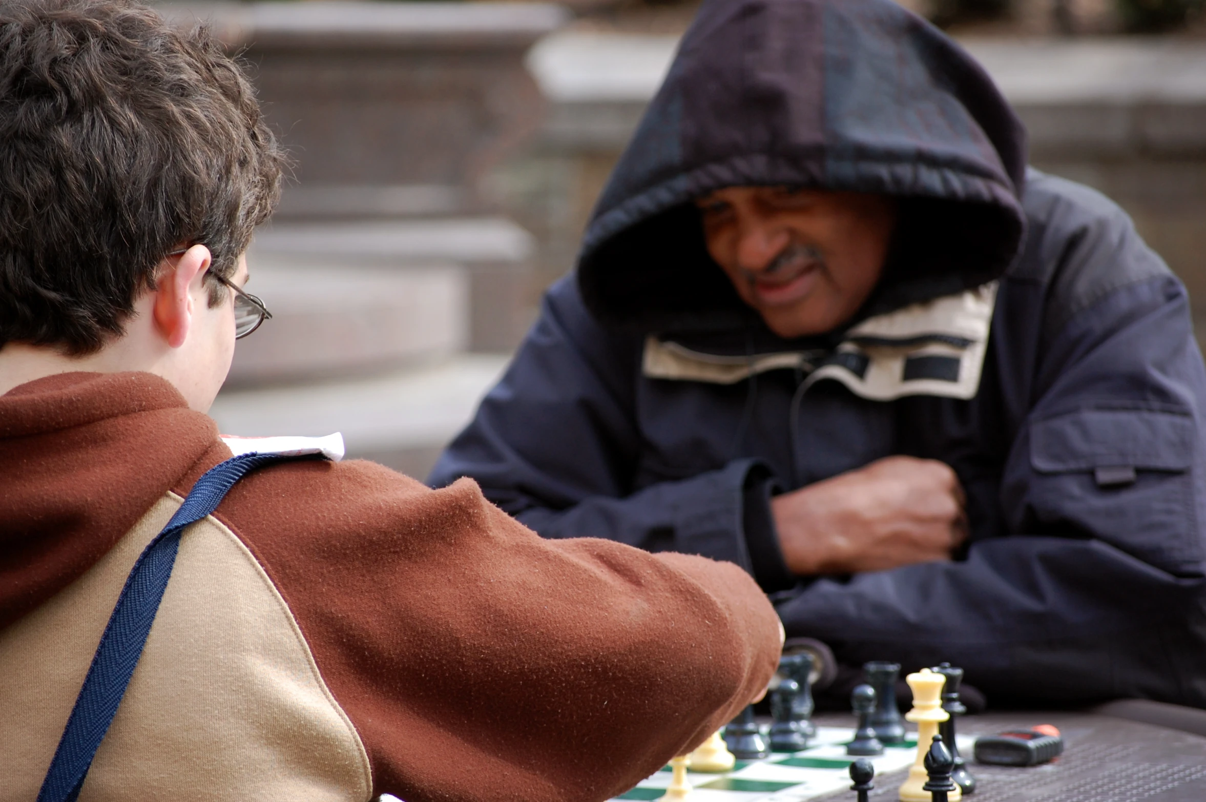 two people playing chess outside on a wooden table