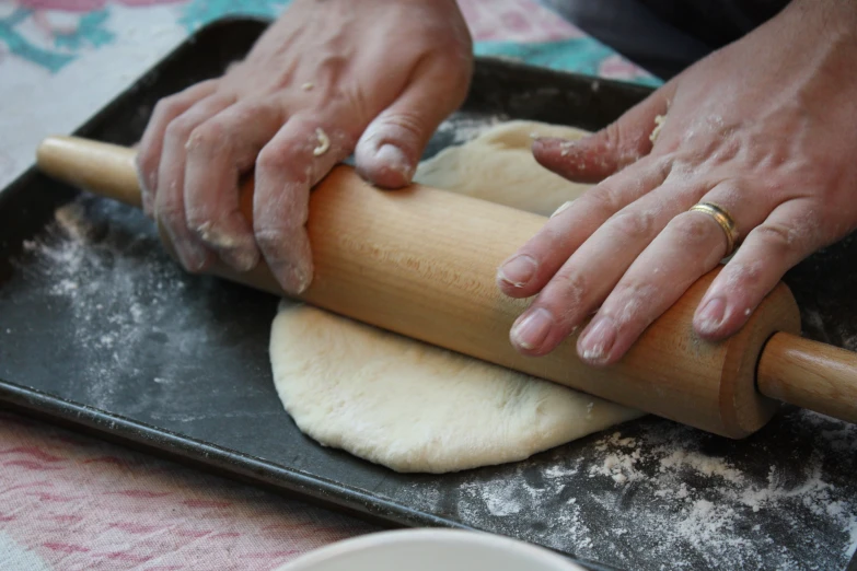 a woman rolling dough into a ball on a metal plate