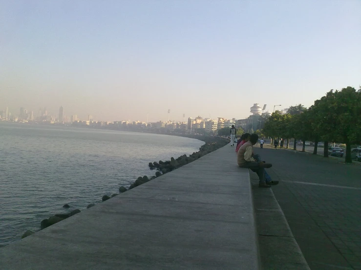 two people sitting on a ledge near the water