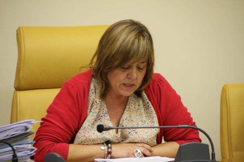 a woman in a red shirt sitting down at a desk with a microphone