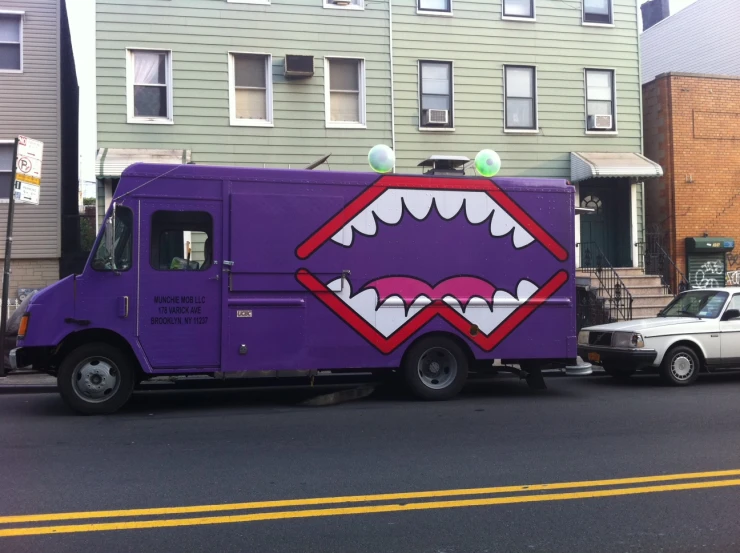 purple truck with mouth painted on back in front of a row of buildings