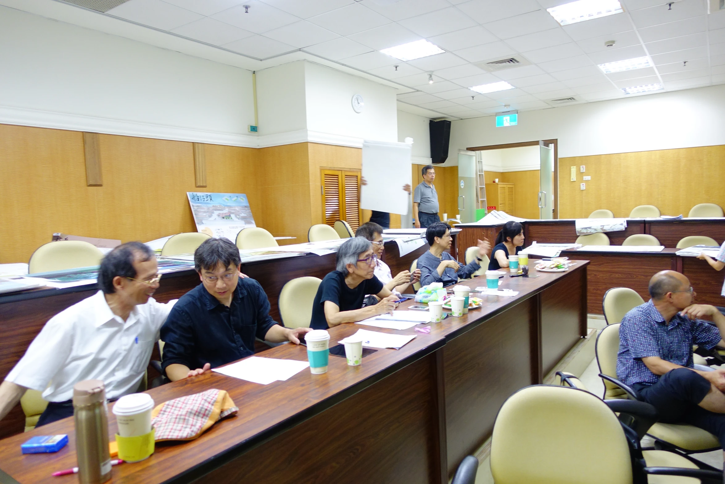 a large meeting room has men sitting at a long table