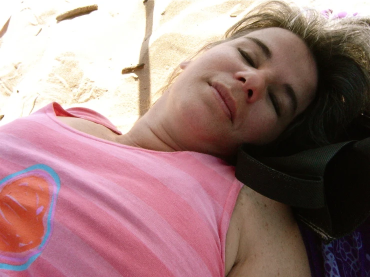 a woman sleeping on a beach wearing a pink shirt