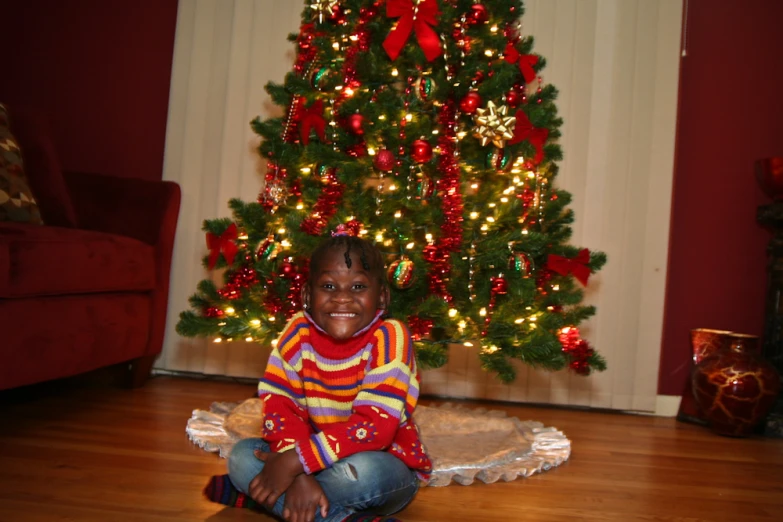 a young child smiling next to a decorated christmas tree