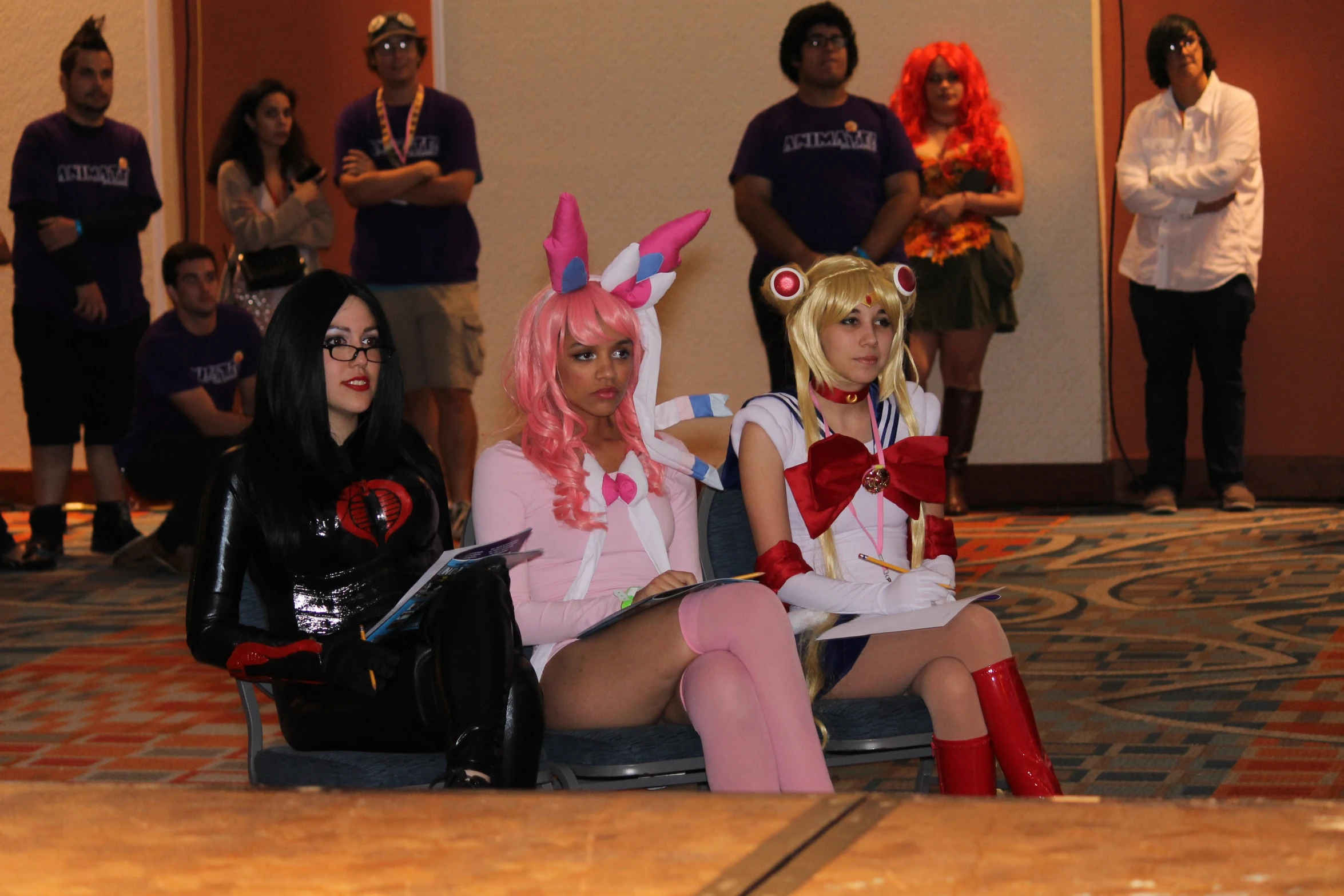 two women in costume sitting on a bench, while a crowd of people stands and look on