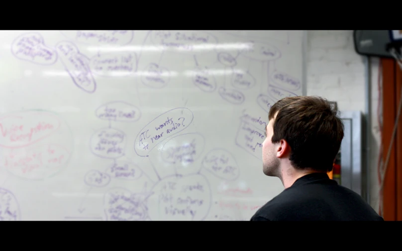 a man in front of a whiteboard covered in writing