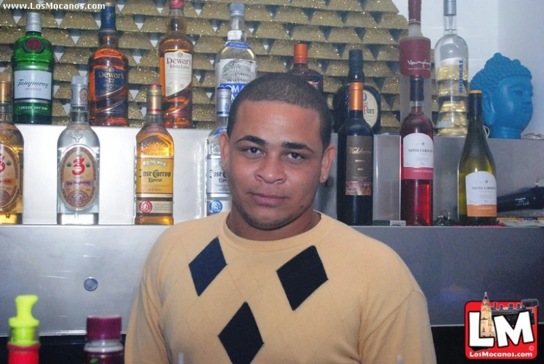 a man in an ugly sweater stands in front of liquor bottles