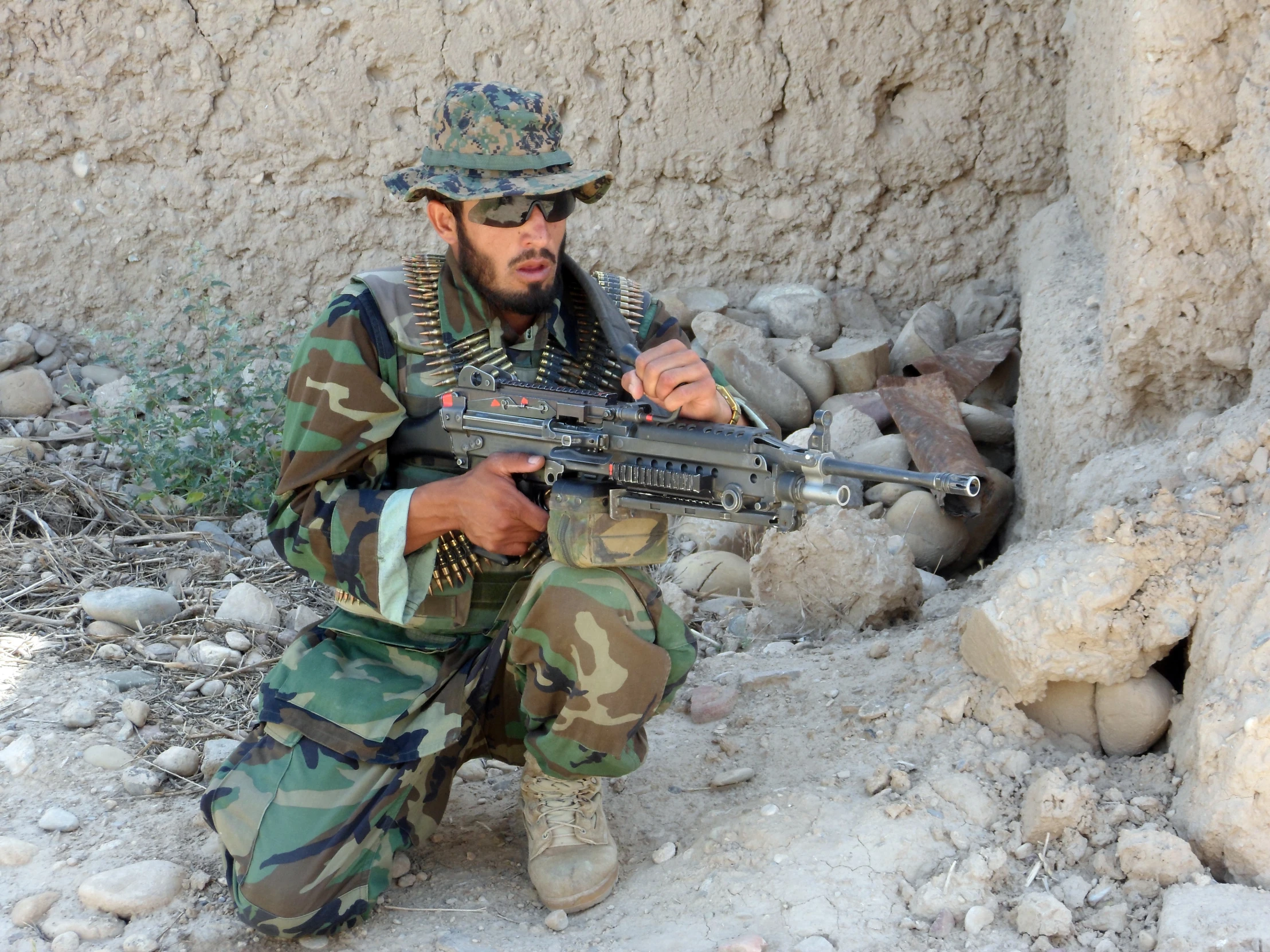 a soldier with a gun, squatting near some rocks