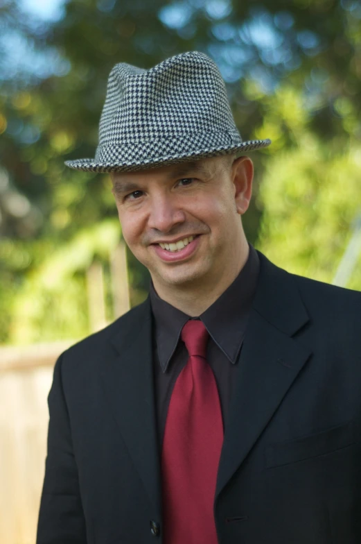 the man wearing a red tie and a gray hat smiles