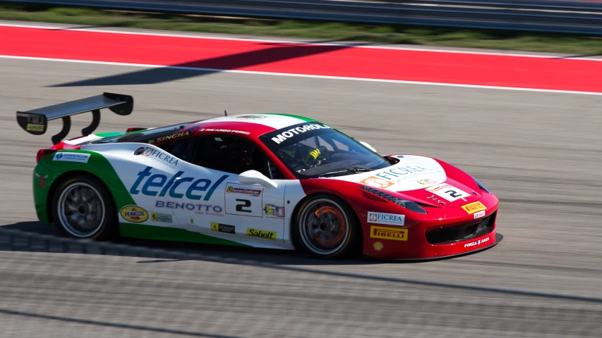 a car drives on a race track as another person stands by the car