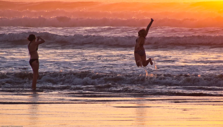 two people are playing in the water at sunset