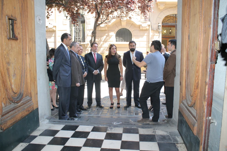 a group of men and women are chatting while standing outside a building