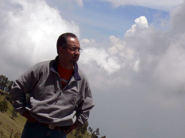 a man with glasses standing on a hill side