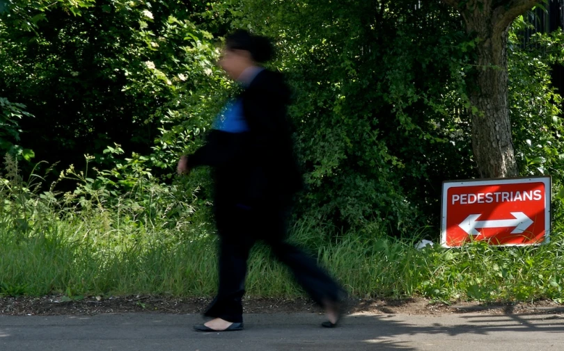 a woman walking down the road past a sign for a pedestrian