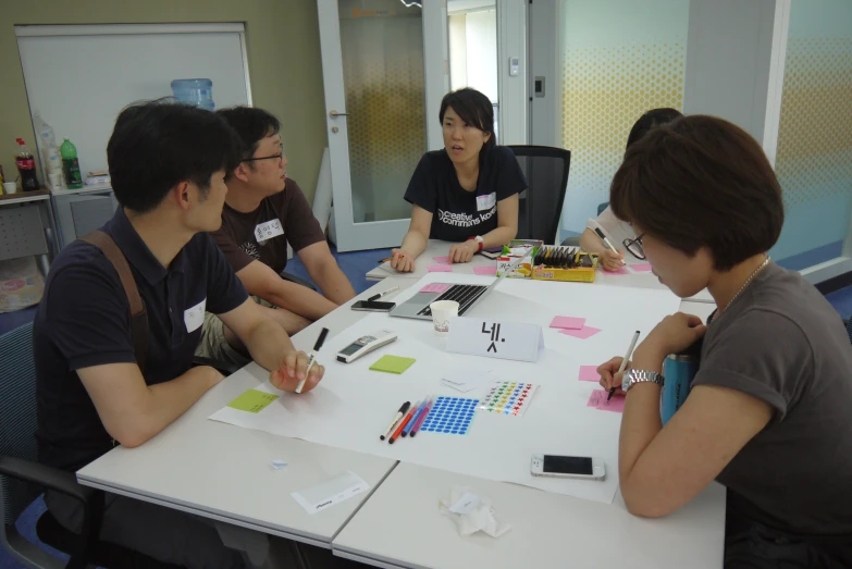 four people are sitting at a table with some pens and note paper