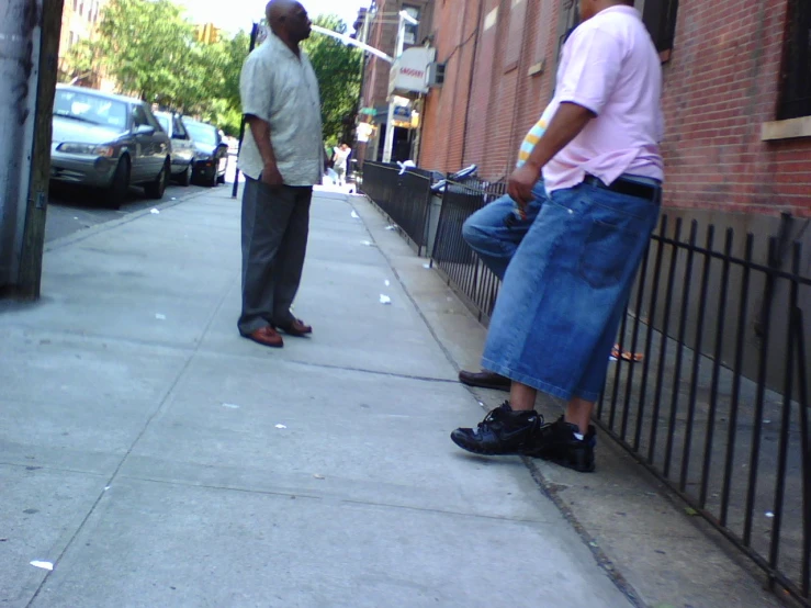 two men are standing on a sidewalk by the fence