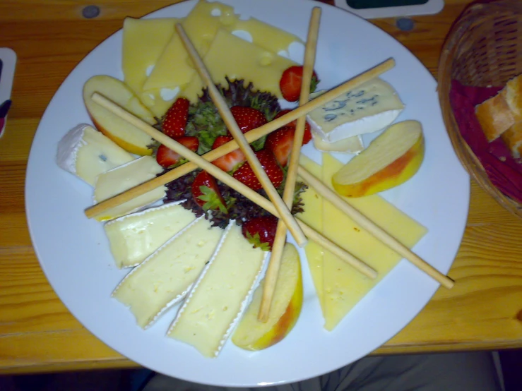 assortment of cheeses, fruits, and bread sticks arranged on white plate