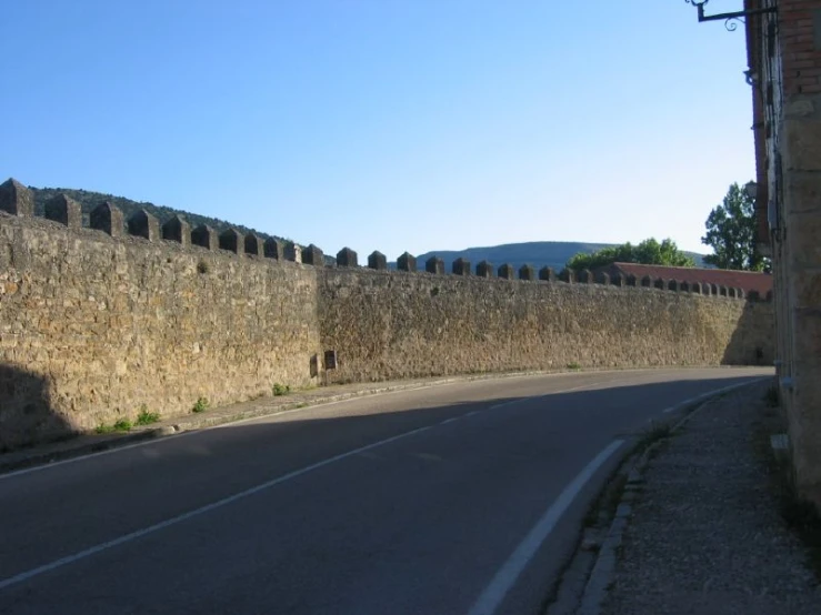 an empty street with a long stone fence next to it